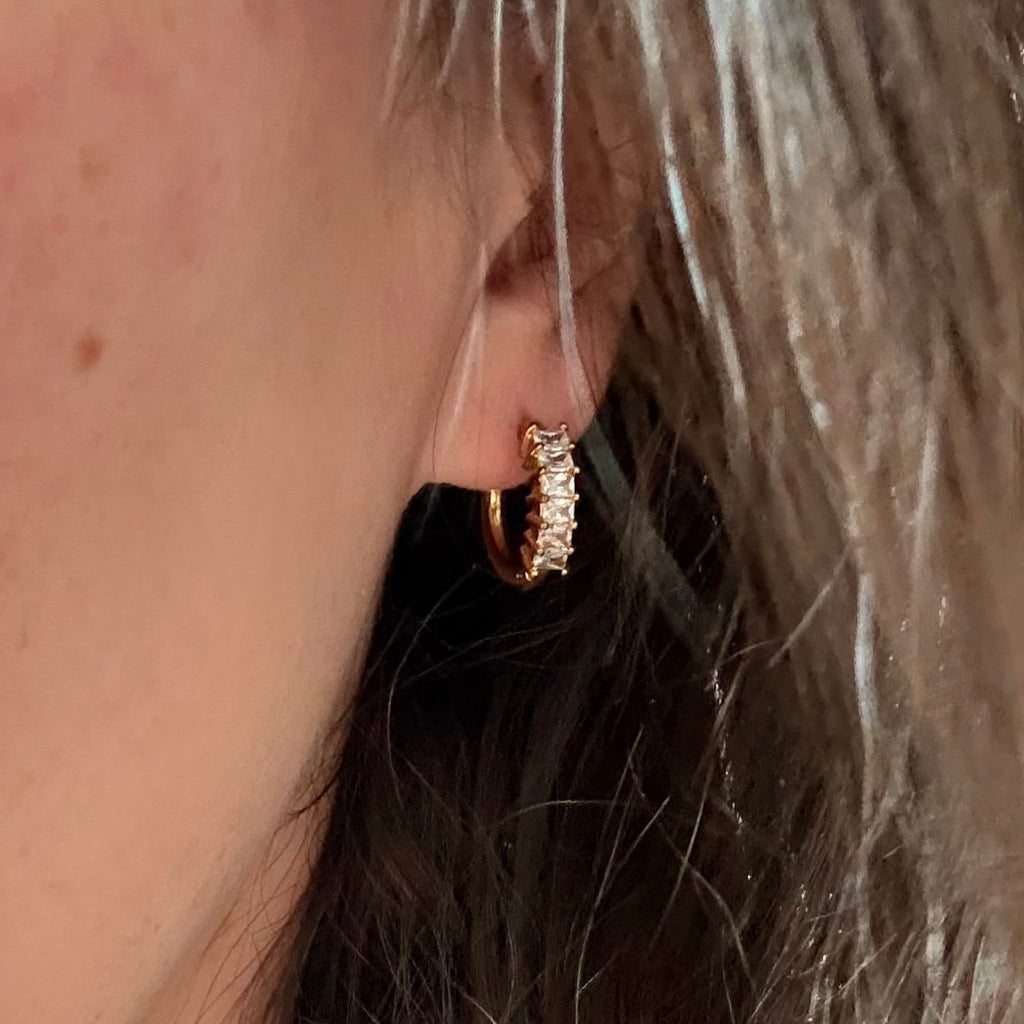 Close-up of a person wearing a gold hoop earring with small cubic zirconia diamonds.