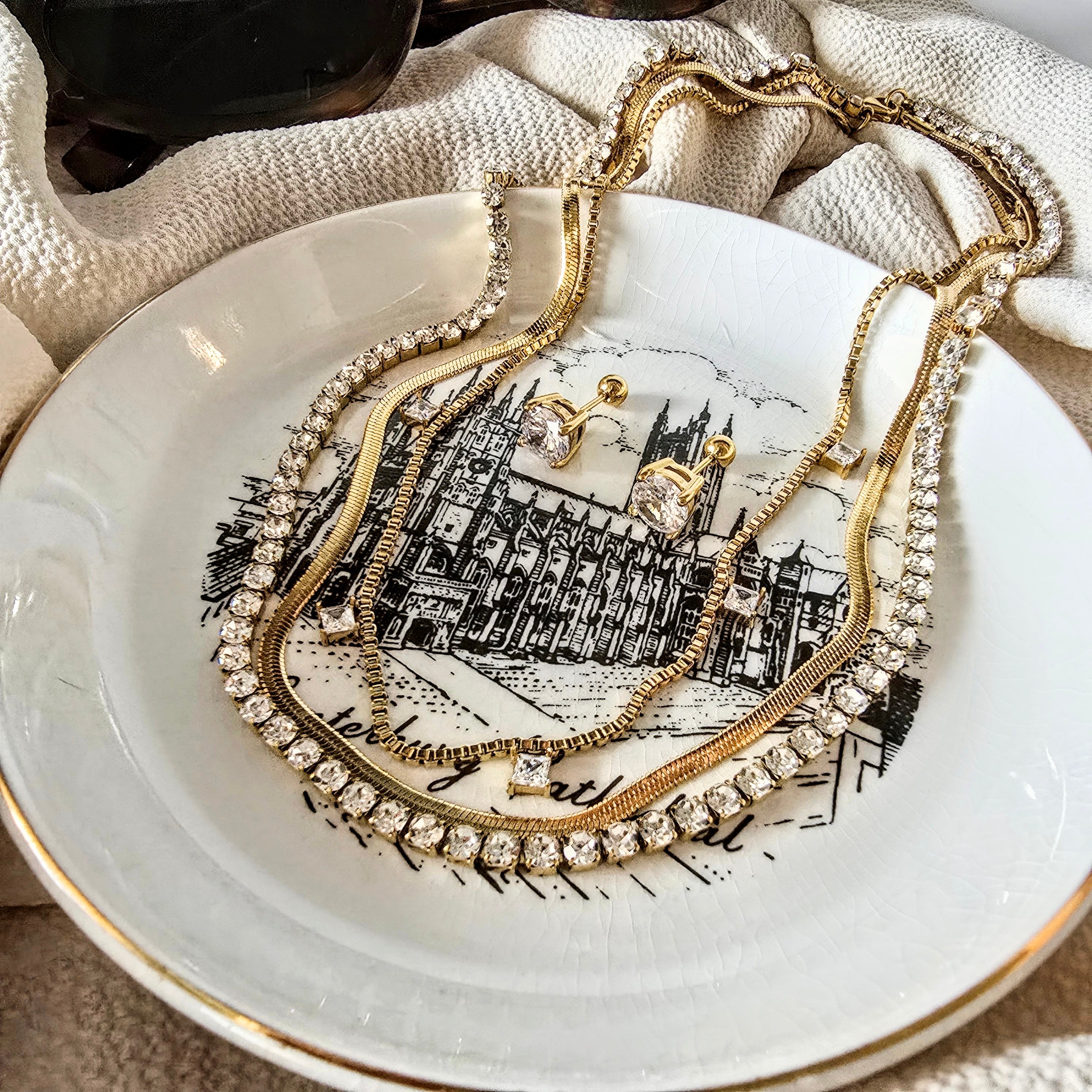 flatlay on plate of three-layered necklace with cubic zirconia diamonds and herringbone chain necklace. triple layered necklace gold, zirconia layered necklace, gold layering necklace
