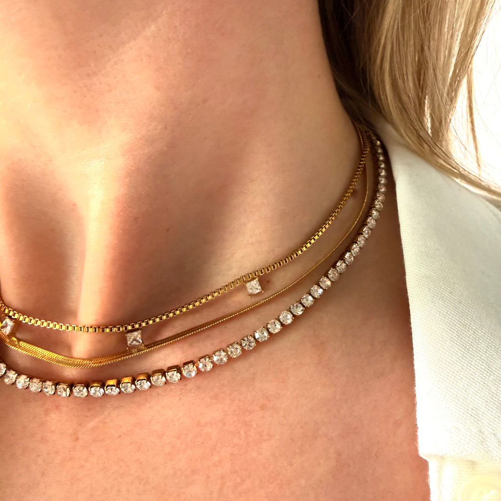 Close-up of a person wearing multiple gold necklaces with cubic zirconia diamonds and herringbone chain necklace. triple layered necklace gold, zirconia layered necklace, gold layering necklace