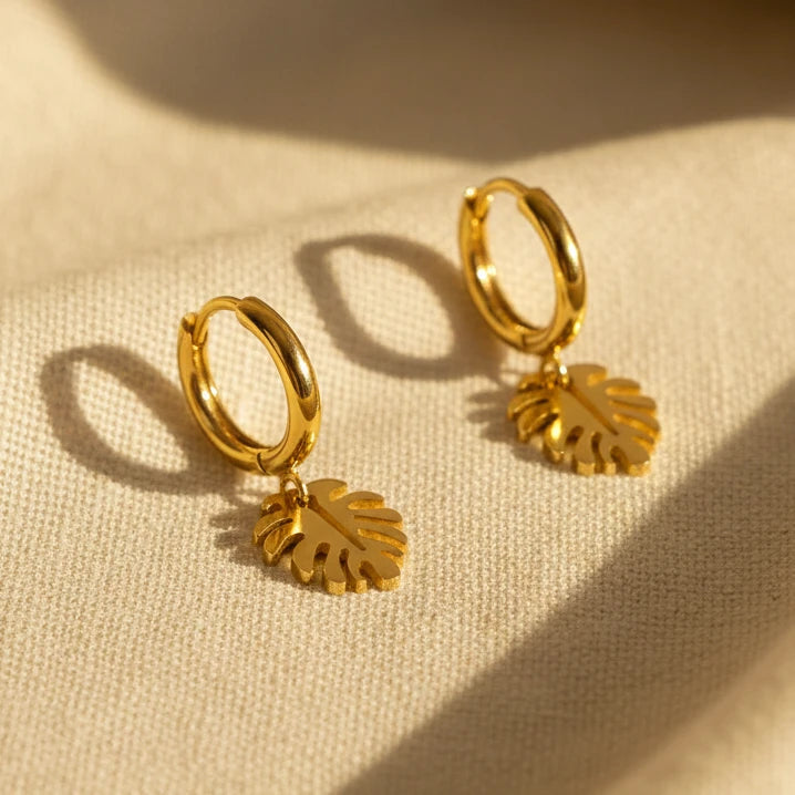 Gold hoop earrings with monstera leaf charms on a white background