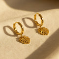 Gold hoop earrings with monstera leaf charms on a white background