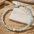 Necklace with natural turquoise irregular stone and a natural pearl laying on sand and marble. natural stone pearl choker, pearl choker necklace gold, beaded choker necklace