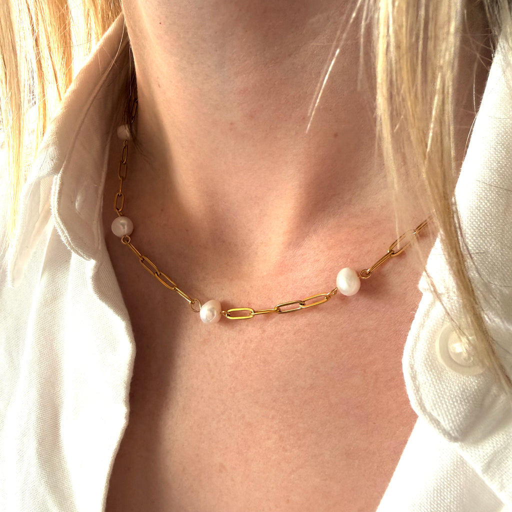 Gold chain necklace with pearl pendants worn by a person.