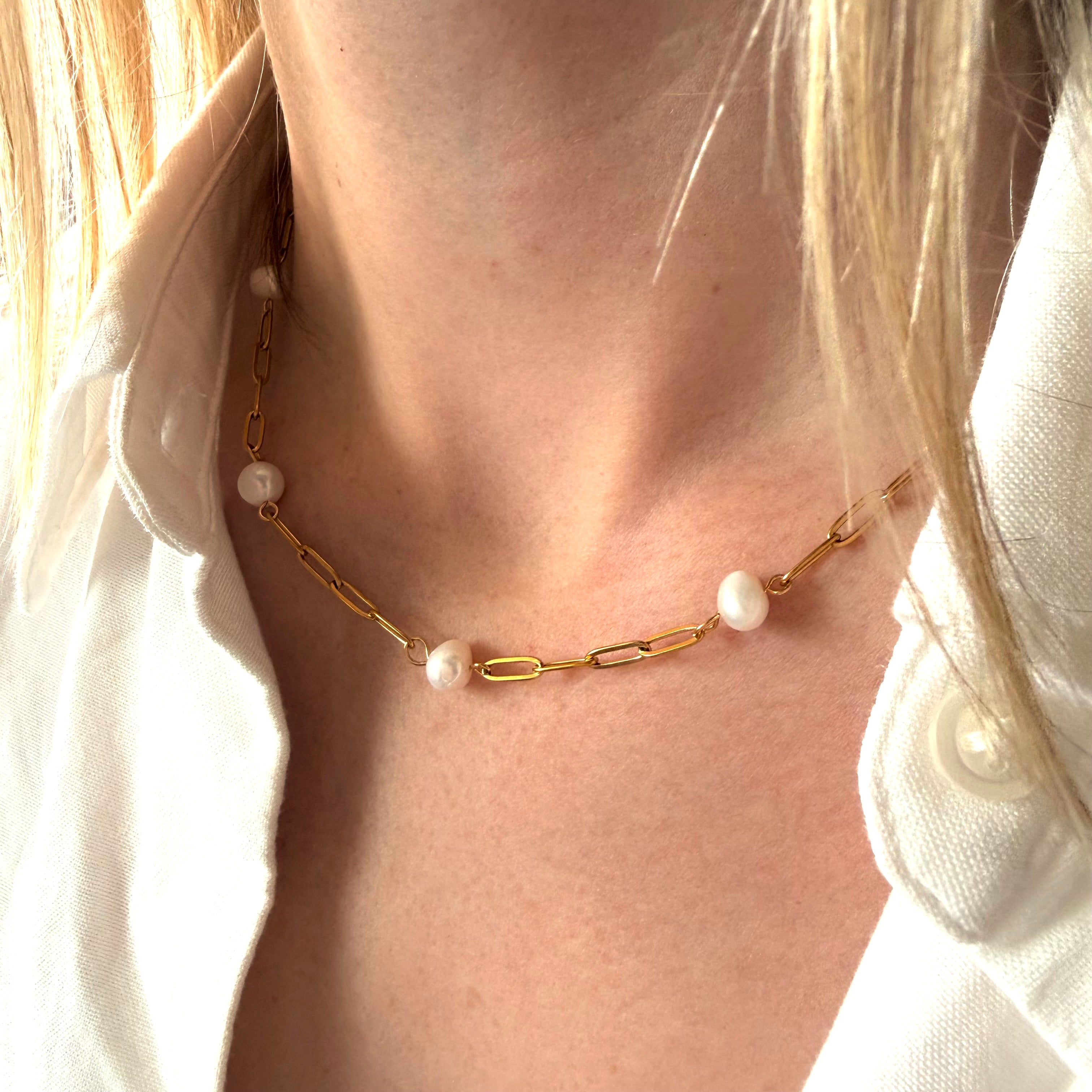 Gold chain necklace with pearl pendants worn by a person.