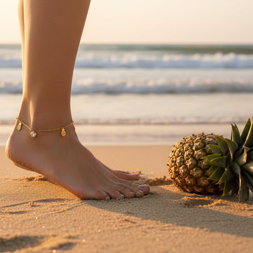 Gold anklet with pineapple and round zirconia charm worn by a woman walking on the beach. PIneapple charm anklet, gold minimalist anklet.