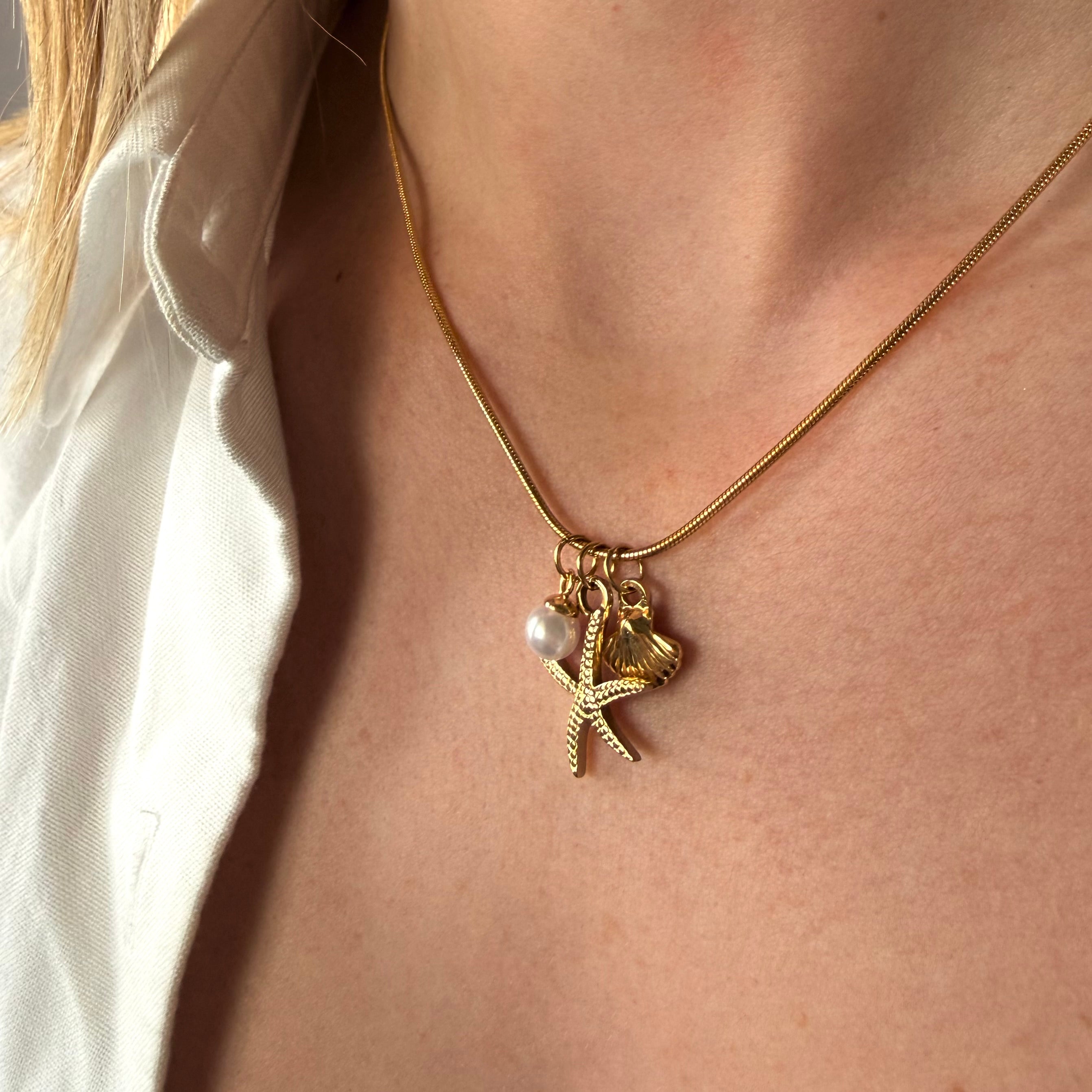 Gold necklace with starfish and pearl charm worn by a person