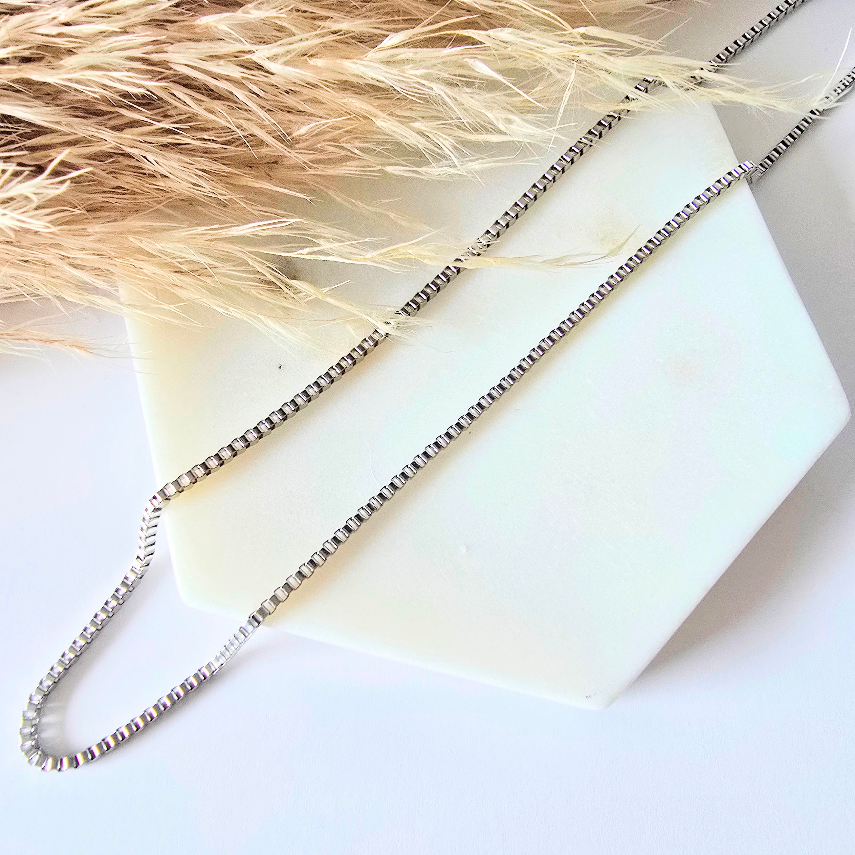 Silver stainless steel box chain necklace on a white stone surface with dried pampas grass