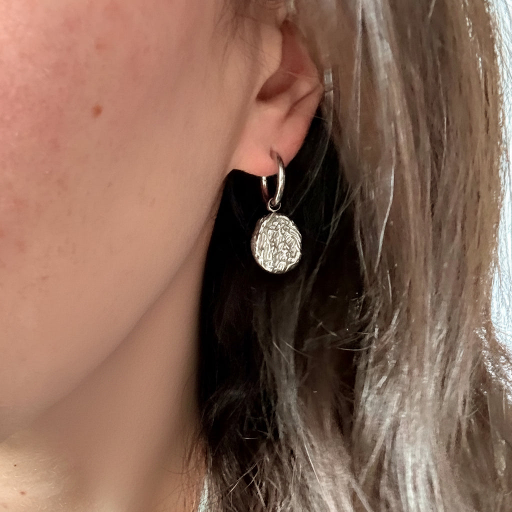 Close-up of a person wearing a silver textured drop earring. silver drop earrings, vintage style earrings, statement drop earrings
