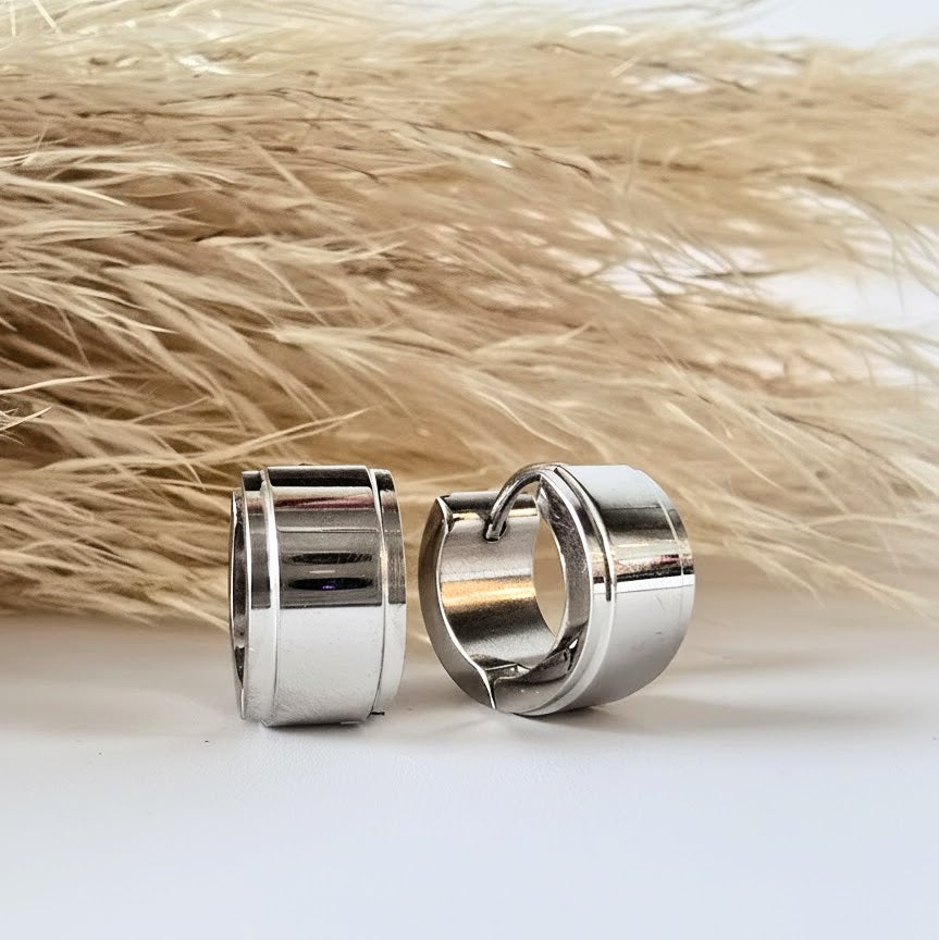 Silver huggie earrings on a neutral background with natural grass texture