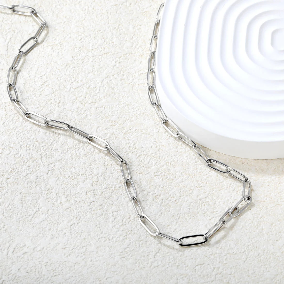 Silver chain paperclip necklace on a textured white surface 