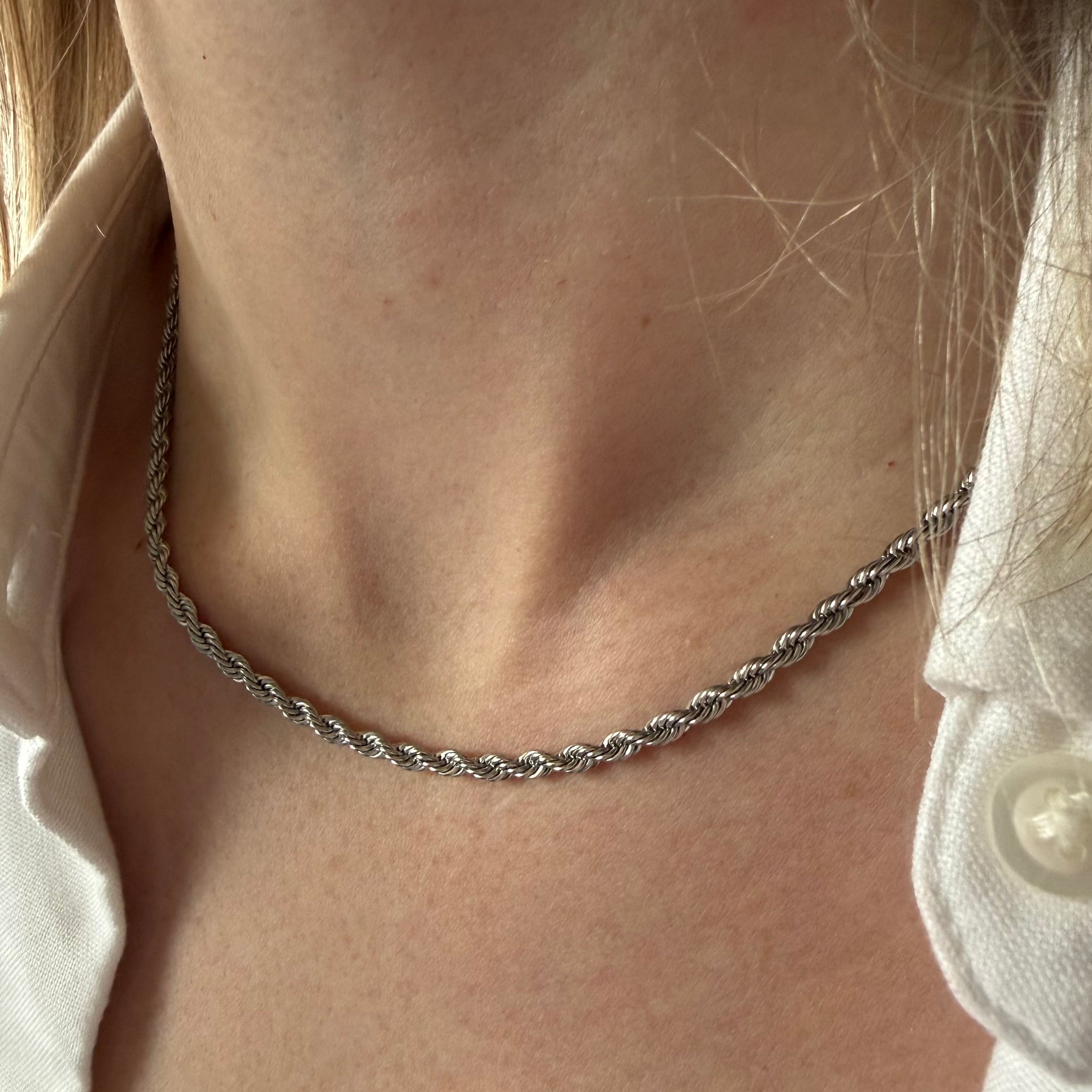 Silver necklace worn by a person with a white shirt. silver rope chain necklace, twisted chain necklace, textured silver necklace