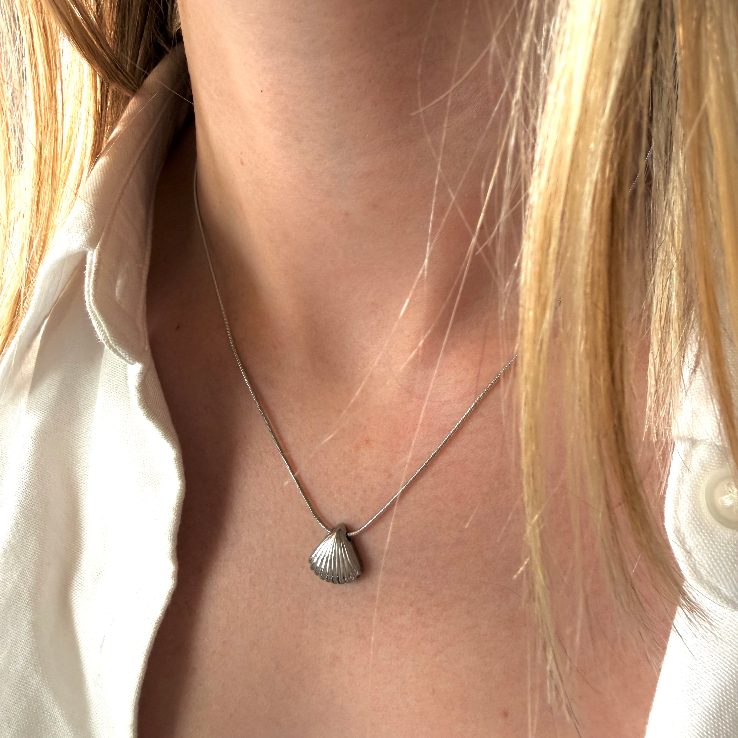 Close-up of a necklace with a shell pendant on a woman wearing a white shirt. Beach Necklace. Ocean inspired jewelry