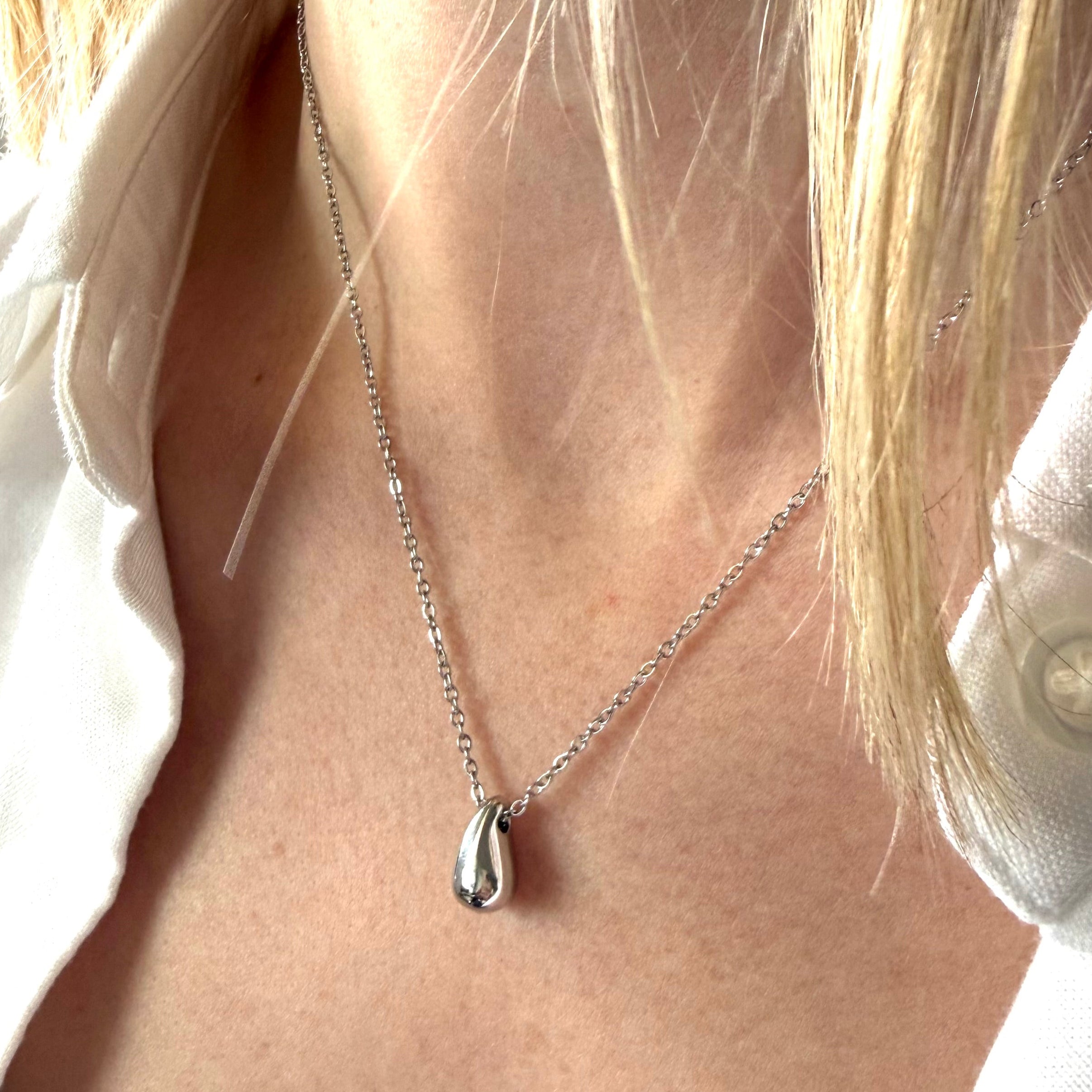 Close-up of a silver necklace with a teardrop pendant on a person wearing a white shirt. teardrop pendant necklace silver, minimalist drop necklace, dainty silver necklace