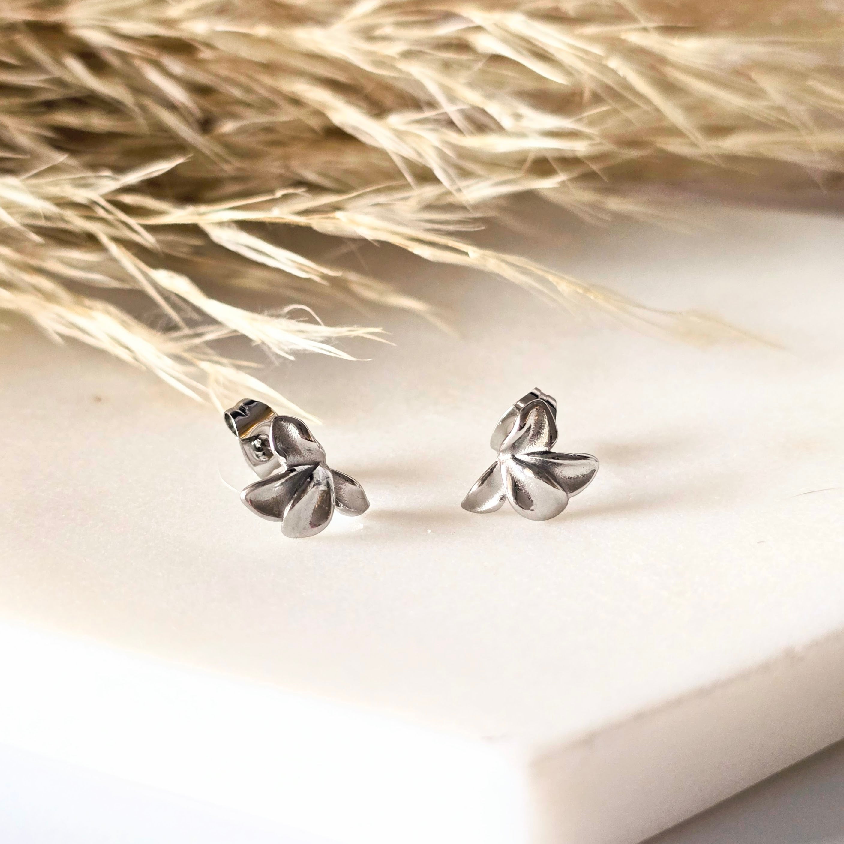 Silver flower earrings on a light background with dried grass