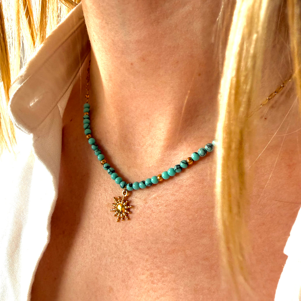 Turquoise stone and chain necklace with a gold sun pendant worn by a person. turquoise sun necklace gold, bead pendant necklace, beach jewelry necklace