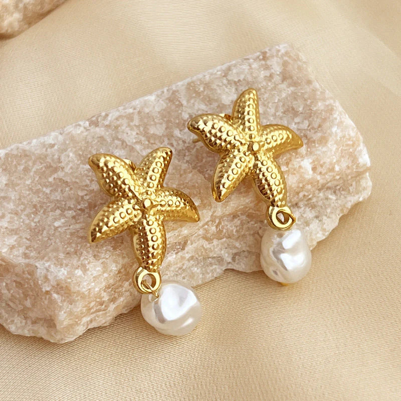 Gold starfish earrings with pearl drops on a beige stone surface. Beach pearl earrings, ocean inspired earrings