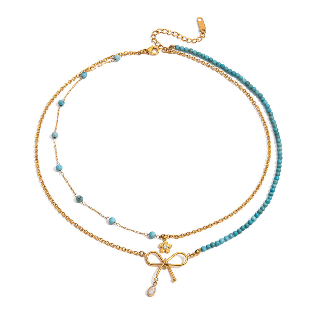 Two layered necklaces with gold and blue turquoise stone beads with a bow and flower on a white background